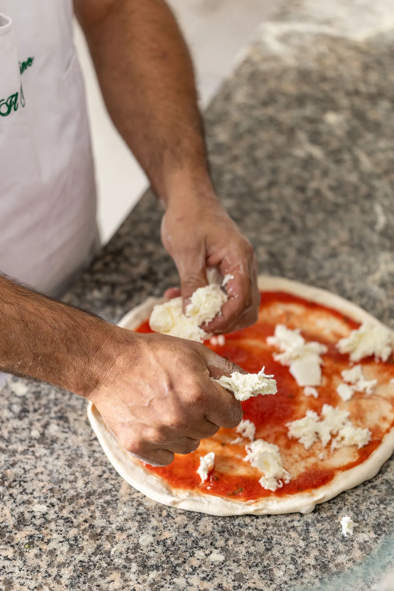 Il pizzaiolo stende la mozzarella sulla pizza