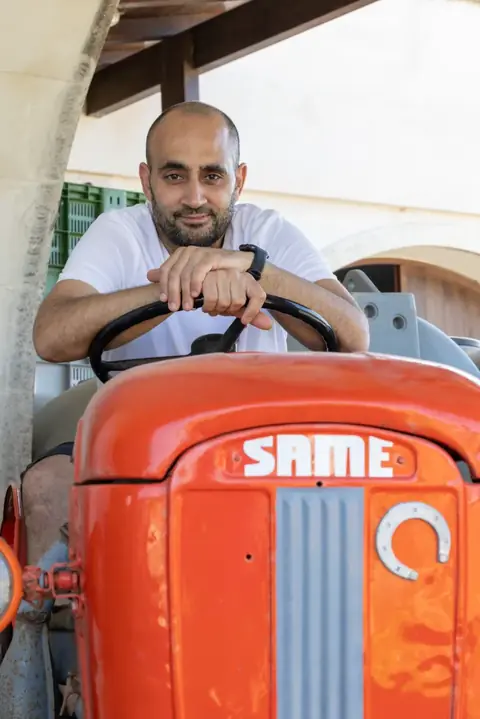 Un uomo sorridente alla guida di un vecchio trattore rosso