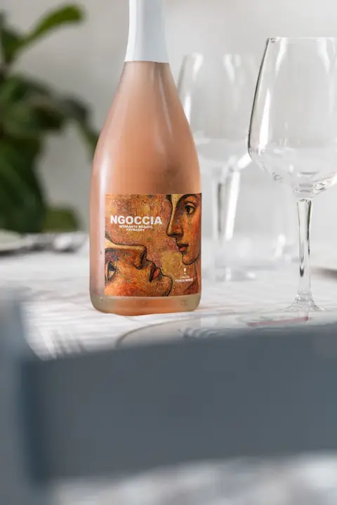 Una bottiglia di rosato con l'etichetta illustrata, tra i calici
