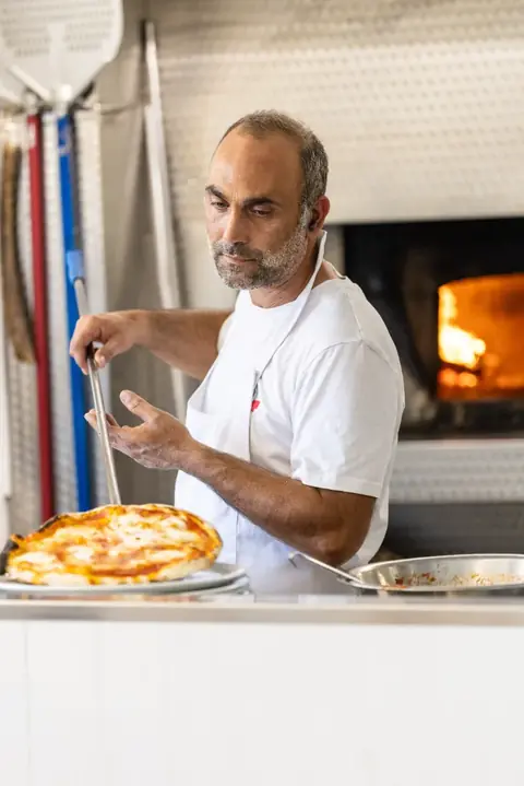 Il pizzaiolo sforna una pizza dal forno a legna