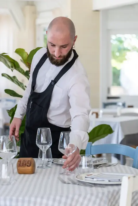 Un cameriere sistema i calici sul tavolo apparecchiato